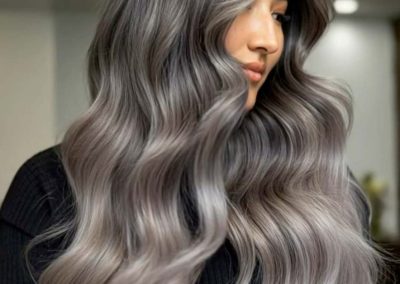 Woman with long, wavy silver ombre hair wearing a black top, in a modern indoor setting.