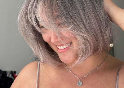 Smiling woman with short, silver-blonde hair in a bob cut, wearing a light tank top and necklace.