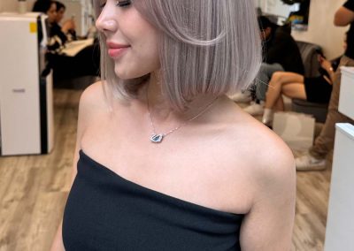 Woman with silver-blonde bob haircut wearing a black strapless dress in a modern hair salon.
