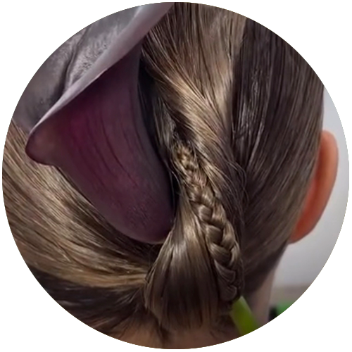 Back view of a woman's braided hair with a large purple flower tucked in.